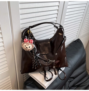Detail of a dark brown glossy leather tote bag with silver hardware and plush pendant