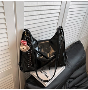 Close-up of black glossy leather tote bag featuring a cute teddy bear charm