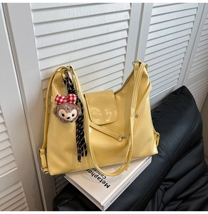 Detail of pale yellow glossy leather tote with logo embossing and plush charm decoration