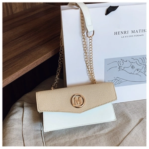 Detalle de bolso bandolera tejido beige con hebilla M dorada y correa de cadena