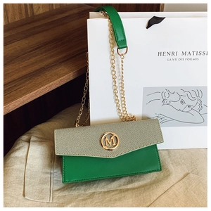 Detalle de bandolera de cuero verde y tejido beige con hebilla M dorada