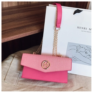 Detalle de bolso bandolera rosa con logo M dorado y correa de cadena de metal