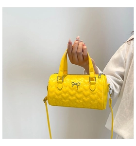 Close-up of yellow heart-quilted cylinder handbag with silver bow hardware detail