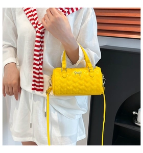 Detail of yellow heart-quilted Boston bag with silver bow charm and adjustable strap