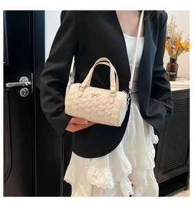 Detail of cream white heart-quilted cylinder bag with silver bow hardware and leather strap