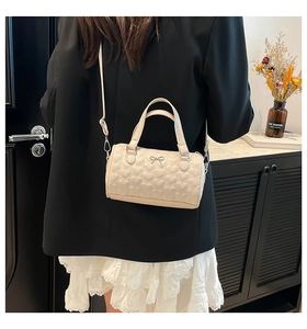 Détail du sac cylindrique crème avec matelassage cœur et nœud porté par le mannequin