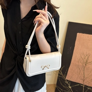 Detail of white leather underarm bag with gold metal bow and dual cord knot strap