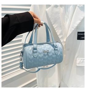 Detail of light blue cylinder handbag featuring heart quilting and silver bow ornament