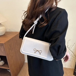 Detailed side view of white underarm bag with golden bow and decorative knotted strap