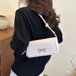 Detailed shot of white leather shoulder bag with gold bow clasp and knotted strap detail