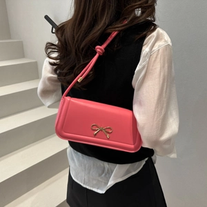 Detailed close-up of a pink leather underarm bag with a gold metal bow clasp