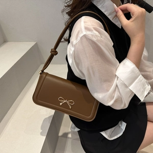 Detail of a brown leather shoulder bag featuring a gold bow accent and slim strap