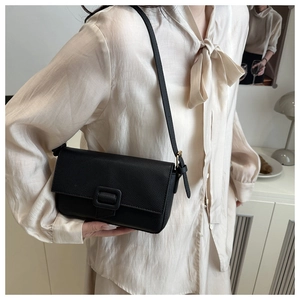 Detail of minimalist black lychee grain leather crossbody bag with square buckle accents