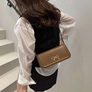 Detailed close-up of brown leather shoulder bag with elegant gold bow buckle