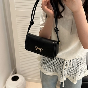 Detailed view of black leather shoulder bag with a gold bow buckle and knotted rope strap