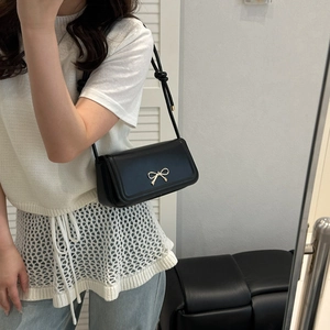 Detailed shot of black leather handbag featuring a delicate gold bow metal buckle