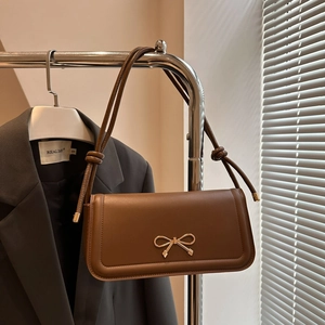 Detailed shot of brown matte leather shoulder bag featuring a gold bow buckle on a suit jacket