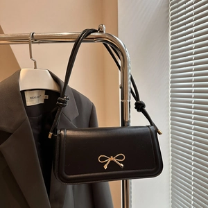 Detail of glossy black leather shoulder bag featuring a gold metal bow clasp and knotted strap