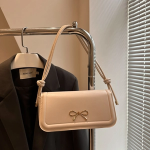 Minimalist cream beige underarm bag with golden bow buckle on a dark grey suit background