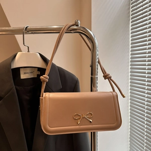 Close-up of beige leather shoulder bag with elegant gold bow metal buckle detail