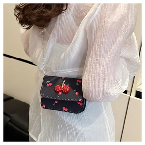 Gros plan d'un sac bandoulière noir avec motif cerises et breloques cerises en relief