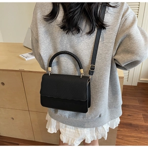 Close-up of black shell shoulder bag with diagonal texture and gold metal hardware