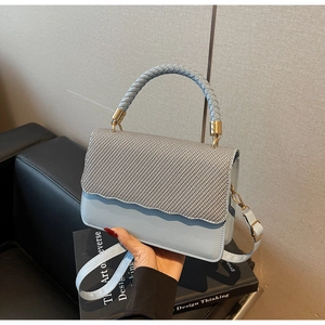 Chic light blue underarm bag with grey woven lid and gold accents on a leather sofa