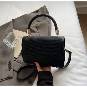 Detail of black textured crossbody bag with twill knit flap and gold hardware accents