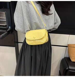 Close-up of yellow saddle crossbody bag in glossy faux leather worn by a model