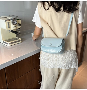 Close-up of light blue glossy leather square bag with buckle detail and thin shoulder strap
