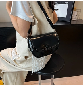 Close-up of black glossy PU leather bag with silver metal hooks and adjustable strap