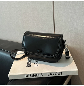 Close-up of black glossy crossbody bag featuring pebbled texture and metal buckle detail