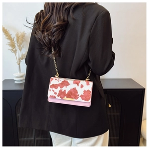 Detail of crossbody bag featuring cow print flap and pink leather with gold chain strap