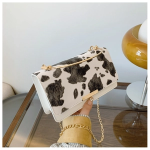 Close-up of cow print crossbody bag featuring gold metal handle and chain strap detail