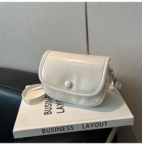 Close-up of cream textured faux leather crossbody bag with round buckle on a book