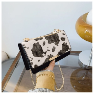 Detail of stylish cow print crossbody bag with gold chain strap and metallic clasp