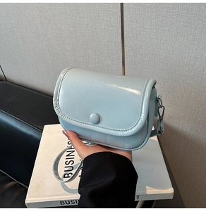 Detail of light blue glossy leather crossbody bag with flap closure and adjustable strap