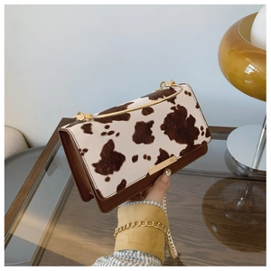 Detail of cow-print pattern flap bag with gold arched handle and chain strap