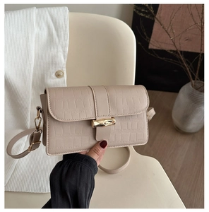 Detail of beige crocodile pattern handbag with golden bamboo buckle in elegant hand-held shot