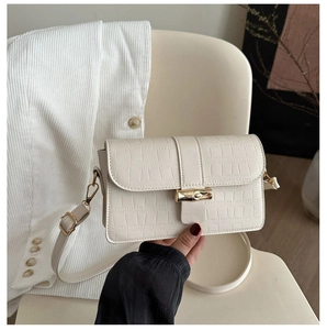 Detail of cream faux crocodile texture and golden bamboo metal clasp on a crossbody bag