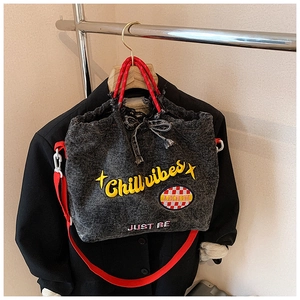 Detail of grey washed denim tote with red handles and yellow Chill Vibes embroidery