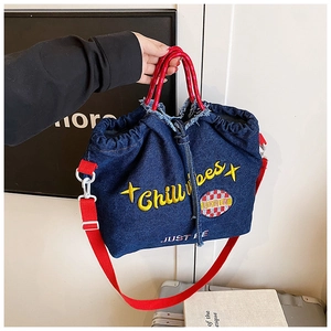 Detail of dark blue denim tote with yellow embroidery and red woven handles