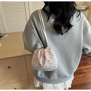 Détail d'un sac seau à fleurs rouges avec bandoulière crème porté par un mannequin