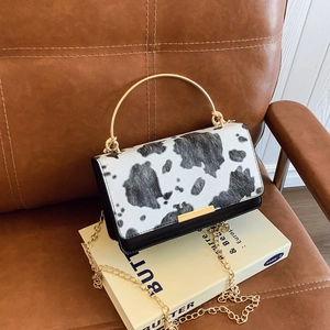 Chic cow print crossbody bag with gold metal handle on a leather seat background