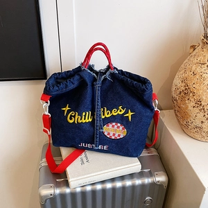 Denim tote bag with Chill Vibes embroidery and red straps on a silver suitcase