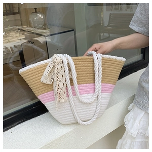 Close-up of tricolor woven straw tote bag featuring rope handles and lace bow detail