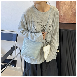 Detail shot of light blue woven bucket bag with crossbody strap in casual urban setting