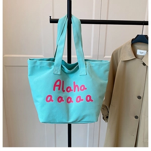 Detail of mint green canvas tote bag featuring pink artistic lettering and double straps