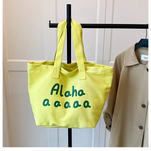 Detailed close-up of lemon yellow canvas tote bag featuring green artistic lettering