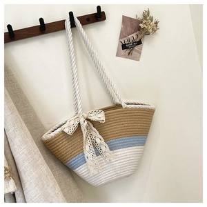 Detail of handmade tricolor woven tote bag with a white lace bow on a wooden hook